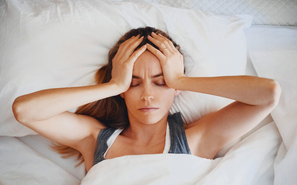 Tired woman in bed, hands on head